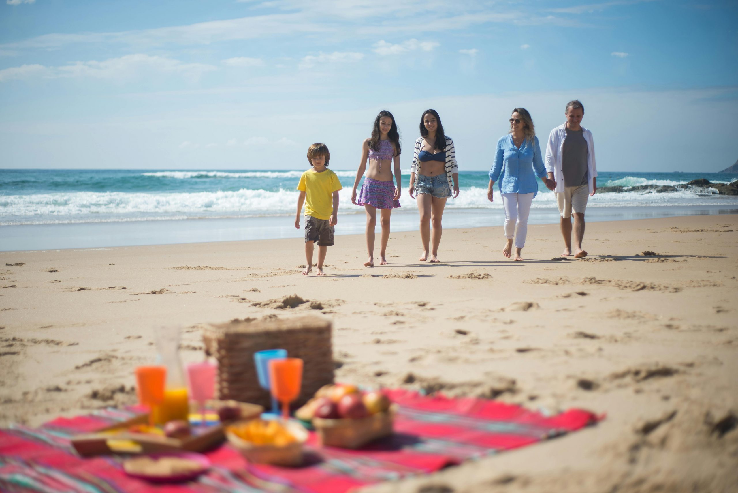 family walking toward a picnic mat laid out on a beach