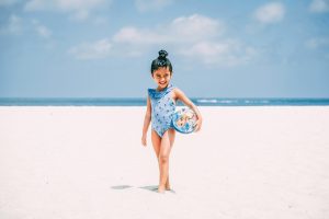 girl in a blue swimsuit smiling while standing on a white sand beach