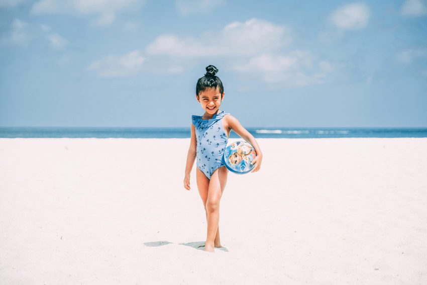 girl in a blue swimsuit smiling while standing on a white sand beach